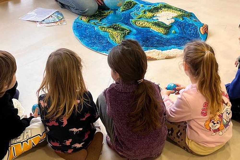 Children sitting around a large tactile relief map of the world with a globe, holding small model globes.